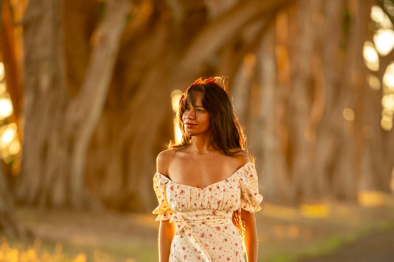 A woman in a floral dress stands on a sunlit forest path, embracing nature's tranquility.